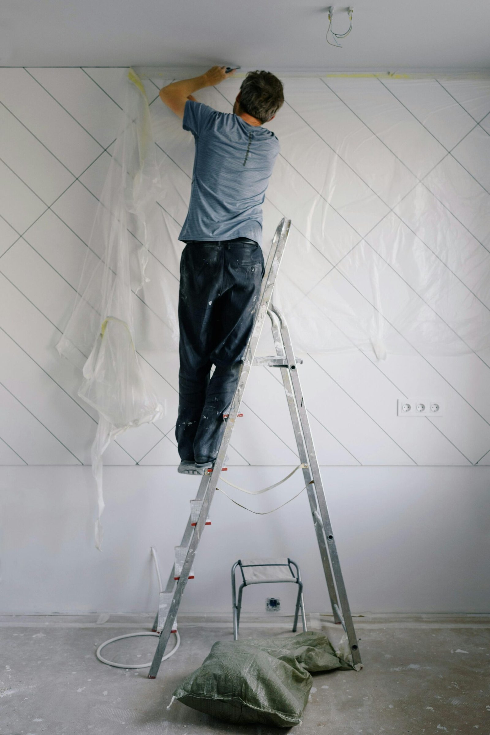 Male house painter on a ladder working indoors to renovate a room.